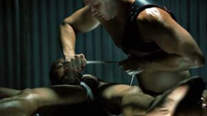 Odin struggles against cuffs, leg shackles and ball gag as he's splayed out to be Brian's next dungeon conquest. Brian's harness glistens black and menacing as he toys with his hot hard prey.